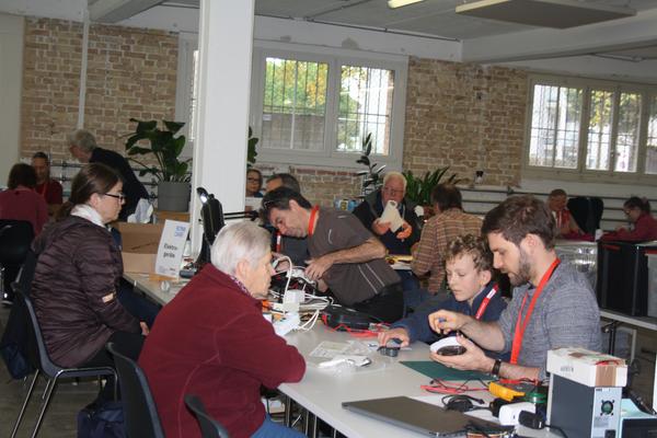 Mehrere Personen sitzen an einem Tisch und reparieren Elektrogeräte.