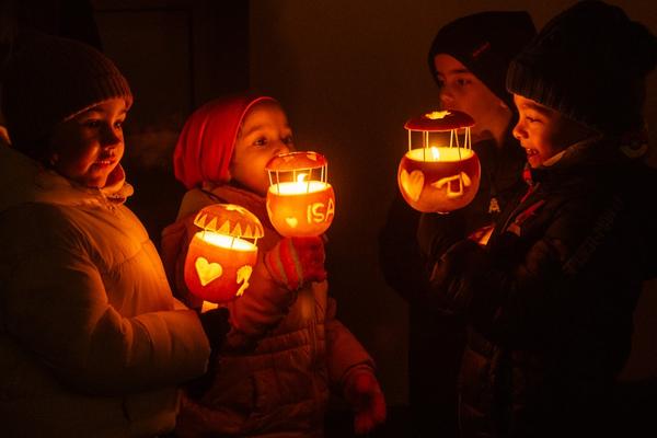 Vier Kinder in Winterkleidung halten bei Dunkelheit beleuchtete Räbeliechtli mit verschiedenen Schnitzereien (Herzen, Buchstaben). Das warme Kerzenlicht beleuchtet ihre Gesichter.