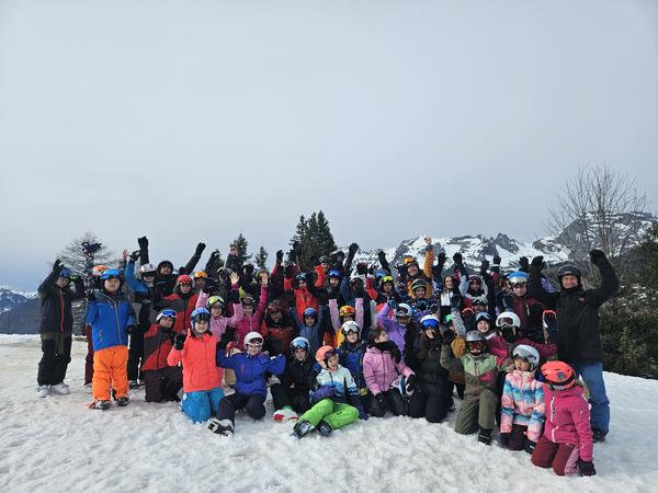 Auf dem Bild ist eine grosse Gruppe von Kindern zu sehen. Sie knien und stehen im Schnee.