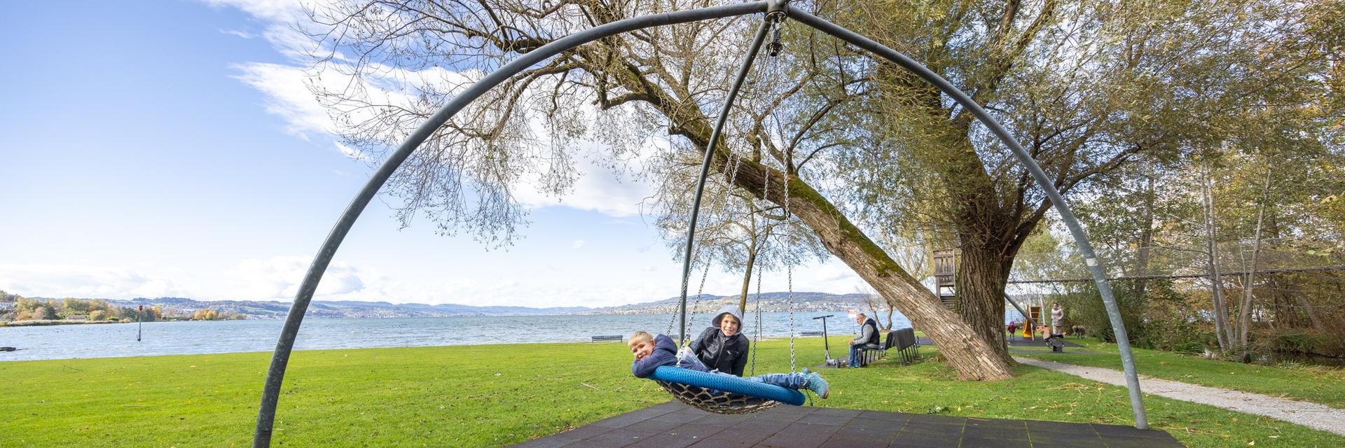 Kinder spielen auf Schaukel auf Spielplatz am See