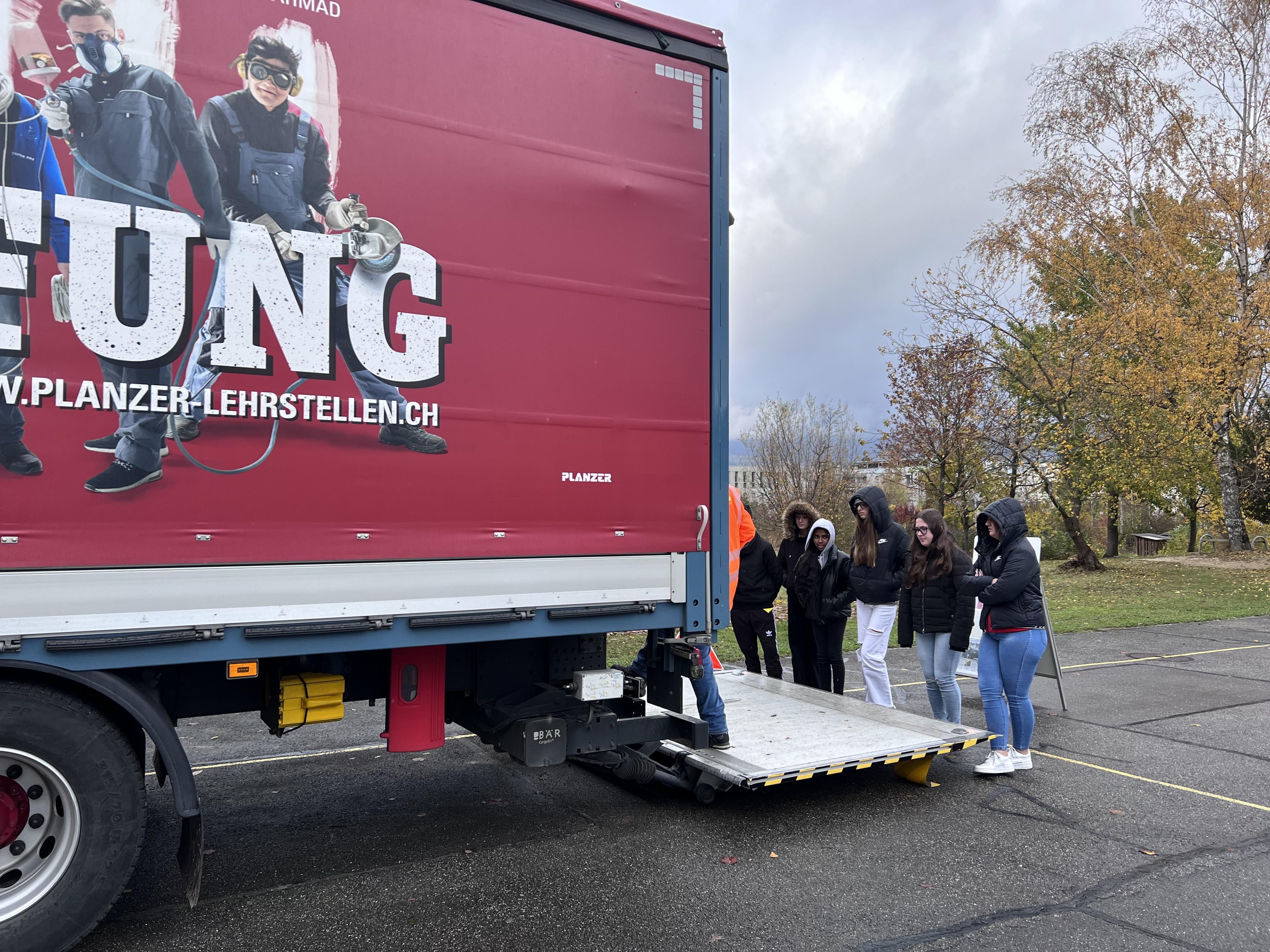 Hier gingen wir in den Lastwagen rein und schauten dort ein Video über den Totenwinkel. Die ganze Gruppe stand auf der Rampe und während dessen wurde die Rampe hochgefahren bis man problemlos auf die Laderampe standen. Drinnen haben wir auf dem Fernseher ein Video angeschaut.