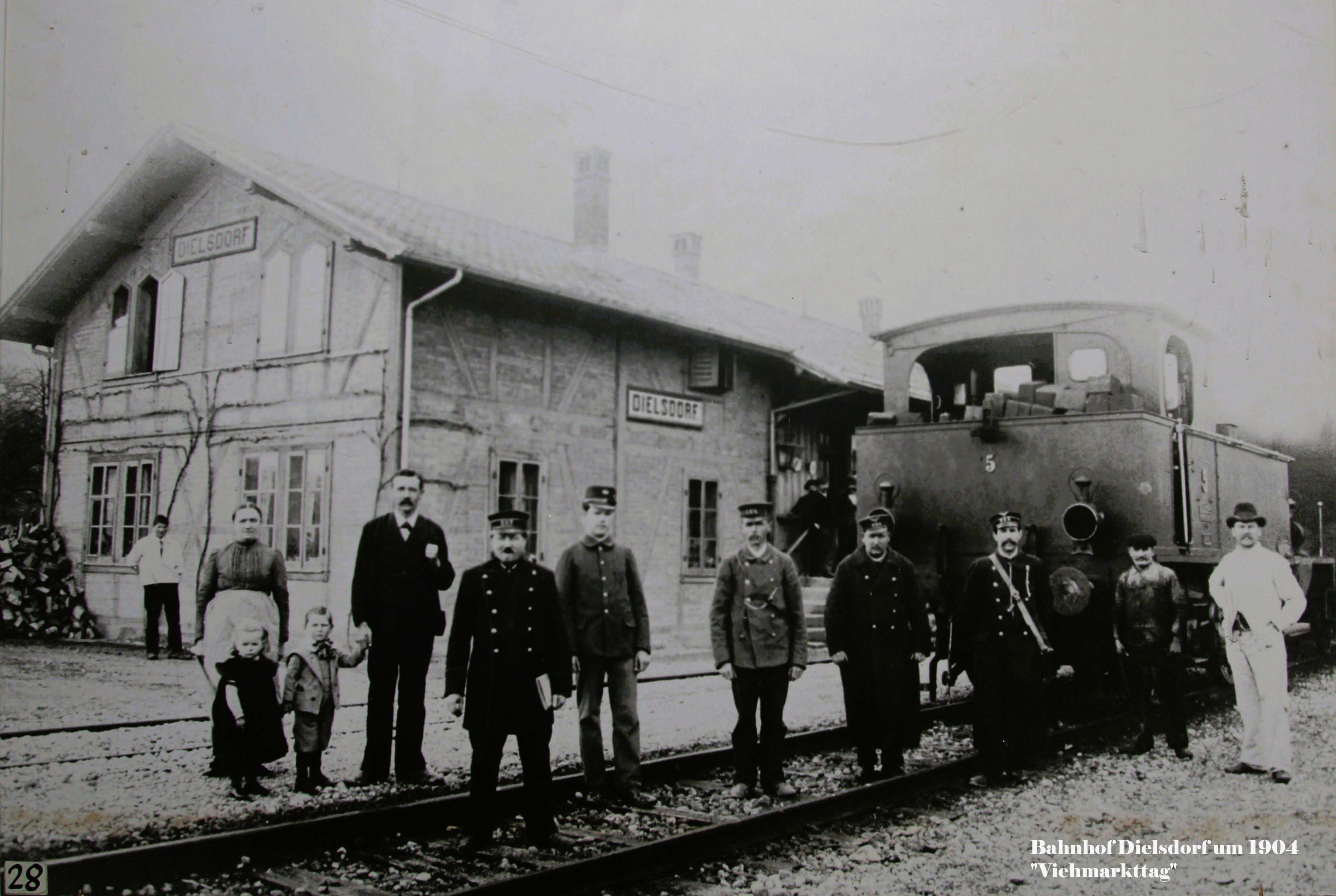 Bahnhof Dielsdorf, um 1904, von Südosten. Viehzug an einem Viehmarkttag vor der Abfahrt; mit Bahnpersonal, Restaurant "Bahnhofgarten", Postbote und Metzgerbursche. Auf der Rampe Chemiker Maag