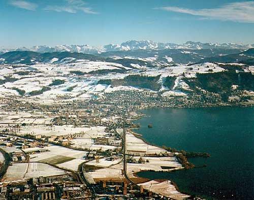 Pfeilgerade führt die Bahnlinie ins Zentrum von Zug. Im Vordergund das Quartier Riedmatt. Hinter dem Zugerberg das Panorama der Glarner Alpen.
