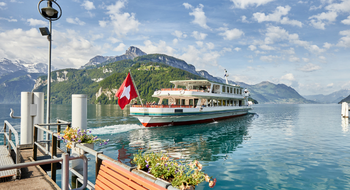 Ein Dampfschiff auf dem Vierwaldstättersee mit einer Schweizerfahne am Heck. 