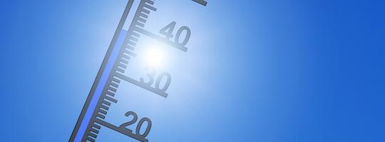 Thermometer vor der Sonne und blauem Himmel