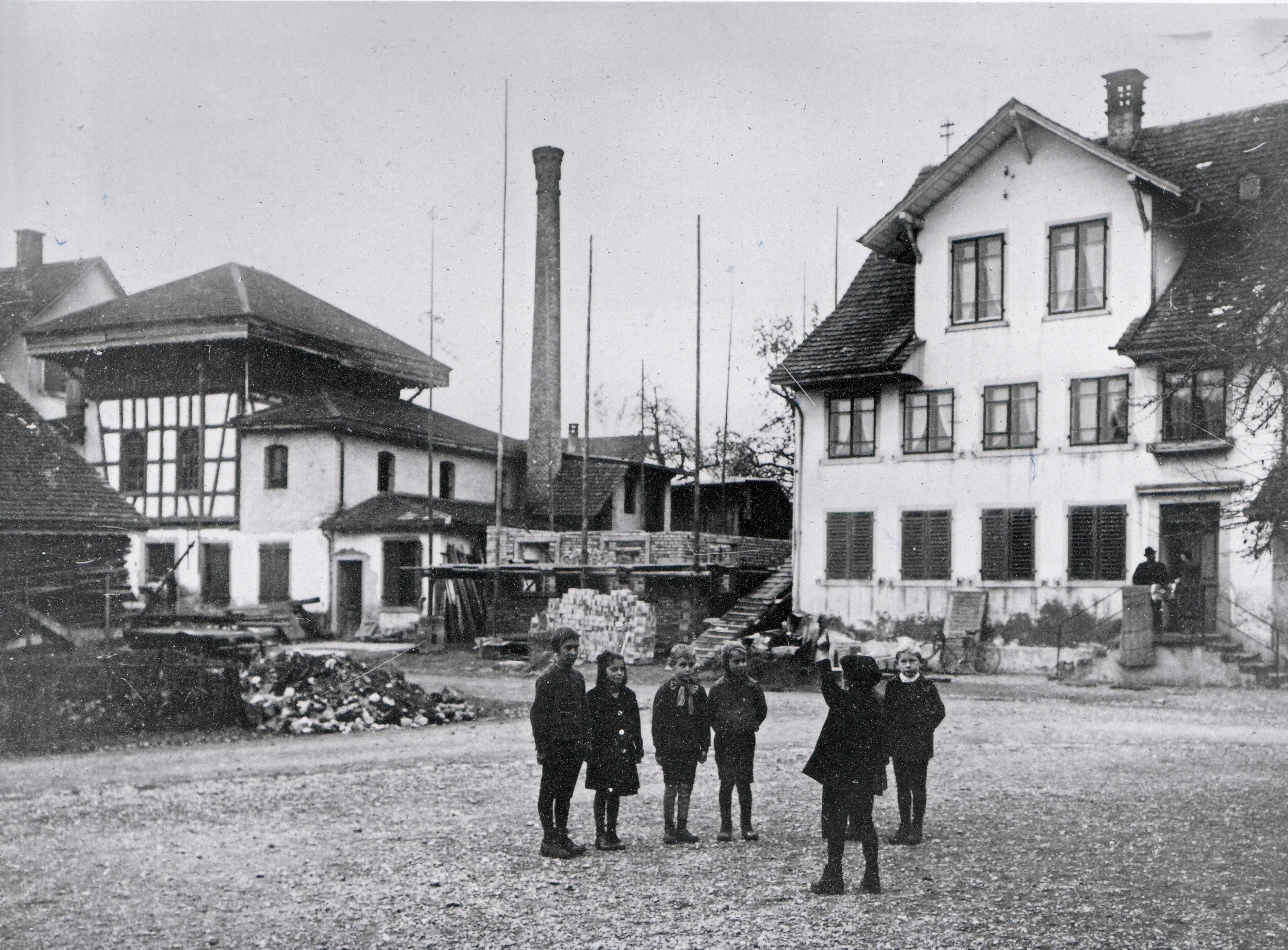 Beim gemeinsamen Spiel der Kinder verwischten die Standesunterschiede etwas. Im Hintergrund die «Limi» mit Kamin und das heutige Gemeindehaus rechts, ehemals Schulhaus mit Lehrerwohnung. Das sogenannte «Kugelhaus» in der Mitte im Neuaufbau.