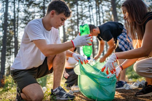 Jugendliche sammeln an einem sonnigen Tag Müll, Plastikflaschen und Papier im Wald.