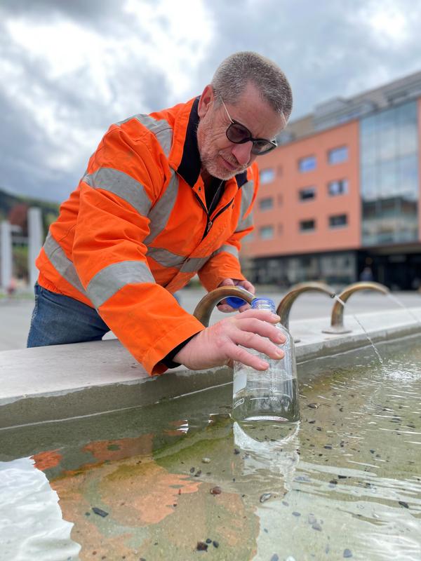 Brunnenmeister Peter Nussbaum befüllt eine Wasserflasche am Dorfplatzbrunnen.
