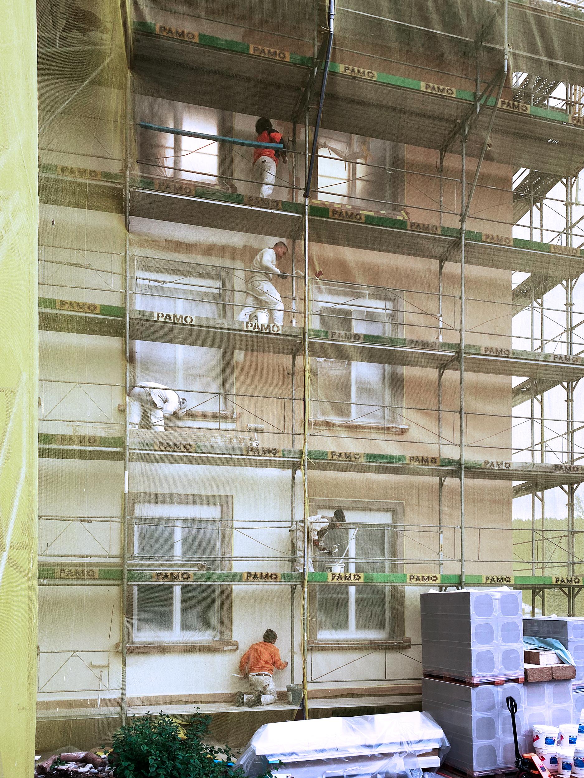 Okt. 2020
Nach der vollendeten Ziegeleindeckung des Hauptdachs kann die Fassade gestrichen werden. Noch kann die neue Fassadenfarbe lediglich durch das gelbe Netz erahnt werden.