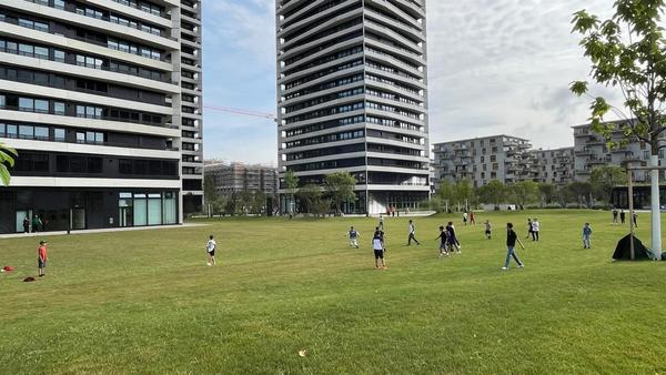 Auf dem Bild ist eine grüne Wiese mit spielenden Kindern zu sehen und im Hintergrund drei Hochhäuser