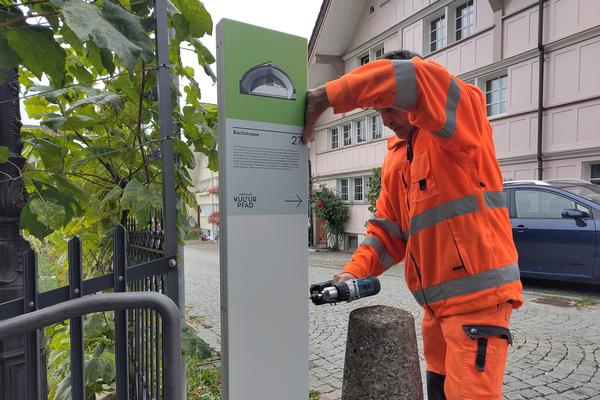 Ein Werkhof-Mitarbeiter schraubt die neue Stele in der Bachstrasse an.