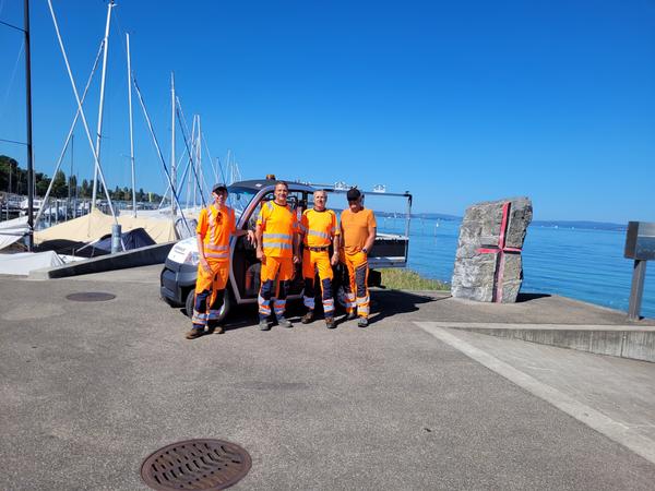 Vier in orange gekleidete Mitarbeiter stehen vor den Elektofahrzeug.
