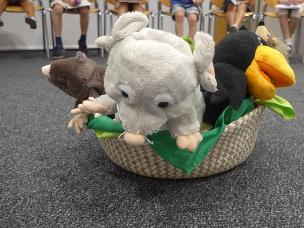 Drei Stofftiere im Körbchen und im Hintergrund baumeln die Beine der Kinder unter den Stühlen