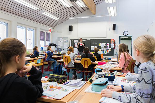 Klasse von hinten, Schüler sitzen in den Bänken, Lehrperson erklärt einen Auftrag