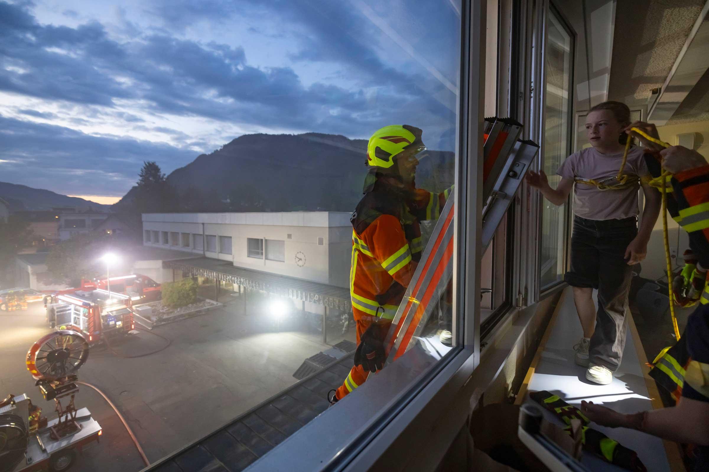 Feuerwehrleute helfen einem Mädchen auf die Leiter.
