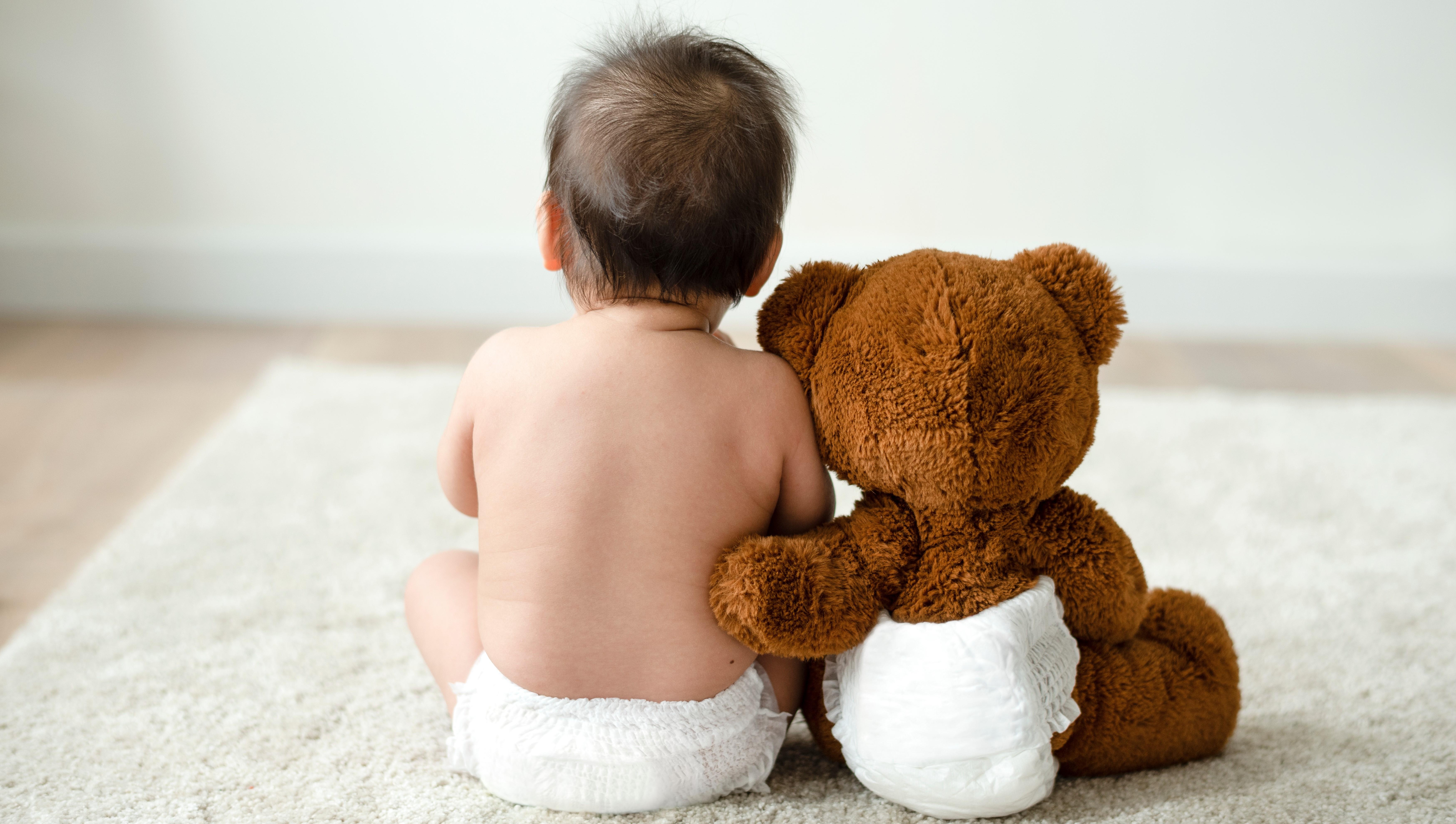 Bild von Kleinkind und Teddybär in Windeln von hinten