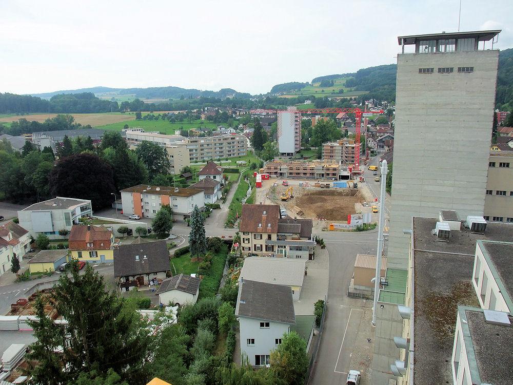 Auf dem Areal des ehemaligen Bahnhofs der Wohlen-Meisterschwanden-Bahn entsteht gerade eine Arealüberbauung mit 45 Wohnungen, Gewerbräumen und zwei Tiefgaragen. Neben der Baustelle der renaturierte Hinterbach. Hinter der Baustelle das schon sehr lange zum Ortsbild gehörende Hochhaus Wohlerstrasse 7. Links die neuen Wohnblocks Wohlerstrasse/Tannwinkel. Im Hintergrund: Der Sandbühl des Ortsteils Hilfikon.