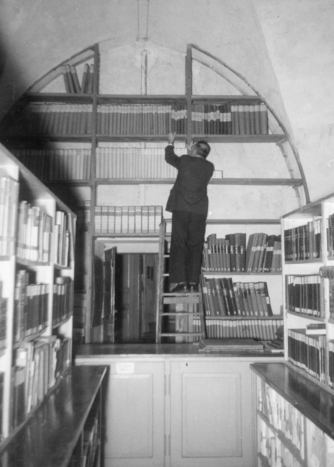 Fotografie des Kanzleisekretärs
Gaudenz Lütscher am Büchergestell
im Gewölbebogen des Stadtarchivs
Chur im Rathaus. (StadtAC, F 01.0215.001,
Foto Caspar, ca. 1928–1935).